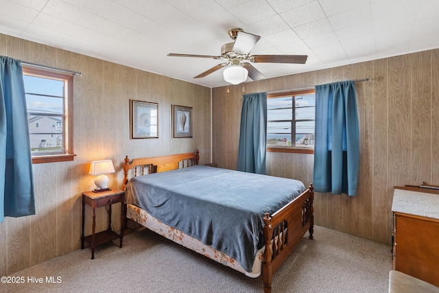 bedroom with ceiling fan, wood walls, and carpet