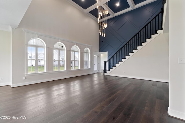 unfurnished living room with a notable chandelier, wood finished floors, a high ceiling, stairs, and crown molding