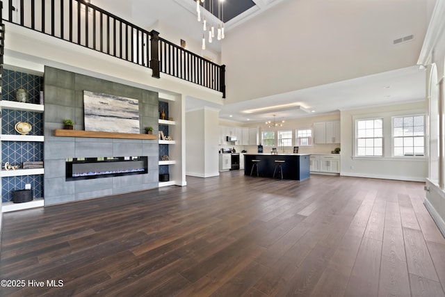unfurnished living room featuring a tile fireplace, dark wood-style floors, a chandelier, and ornamental molding
