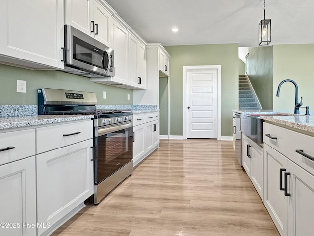 kitchen with white cabinets, light wood-style flooring, a sink, decorative light fixtures, and appliances with stainless steel finishes
