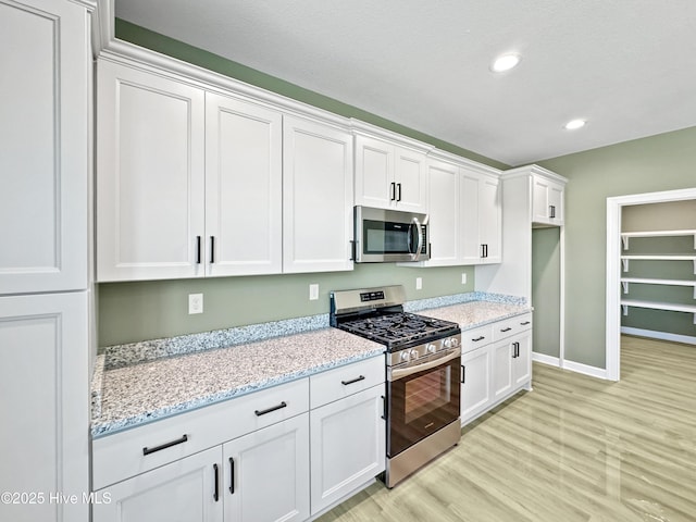 kitchen featuring light wood-style flooring, baseboards, white cabinetry, light stone counters, and appliances with stainless steel finishes