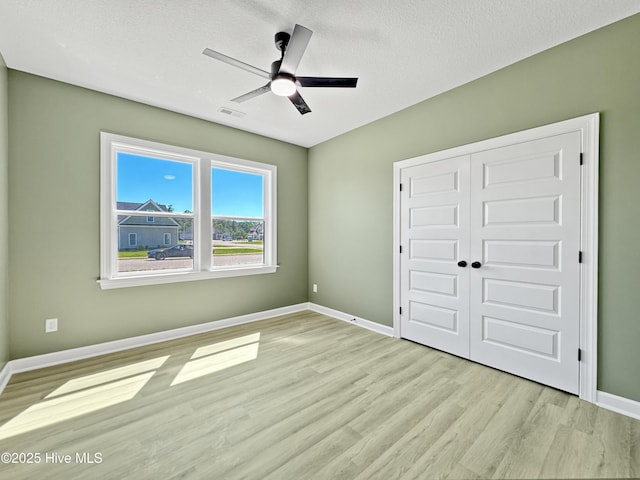 unfurnished bedroom featuring a textured ceiling, wood finished floors, a closet, baseboards, and visible vents