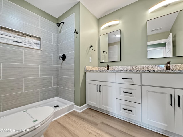 bathroom with a tile shower, double vanity, wood finished floors, and a sink