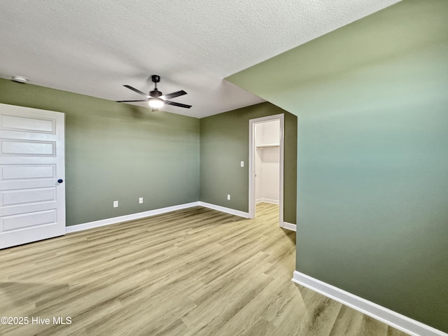 empty room with light wood-type flooring, a textured ceiling, a ceiling fan, and baseboards