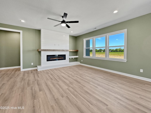 unfurnished living room featuring ceiling fan, baseboards, a large fireplace, and light wood-style floors