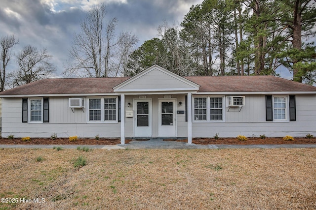 ranch-style house featuring a wall mounted AC, a front lawn, and a shingled roof