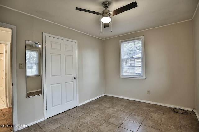 tiled spare room featuring a healthy amount of sunlight, a ceiling fan, and baseboards
