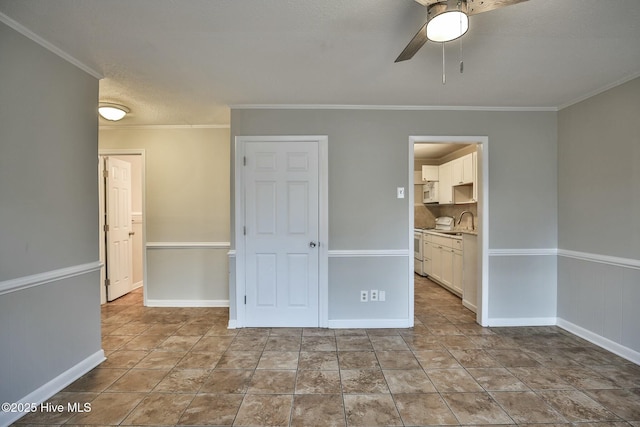 empty room featuring ornamental molding, baseboards, ceiling fan, and a sink