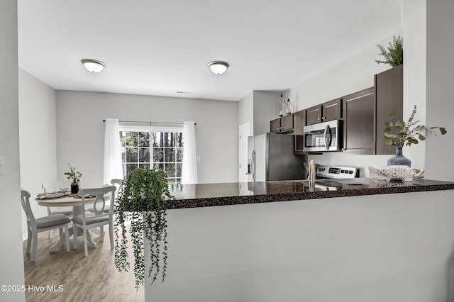 141 Beacon Woods Dr, Holly Ridge, NC 28445 - kitchen featuring stainless steel appliances, dark brown cabinetry, a peninsula, light wood-style floors, and dark stone countertops