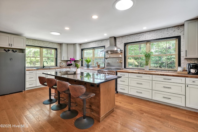 kitchen with freestanding refrigerator, wall chimney range hood, a sink, wood counters, and a kitchen breakfast bar