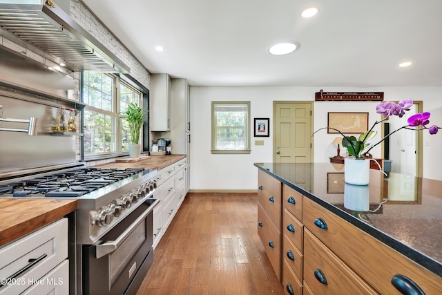 kitchen featuring stainless steel range, white cabinetry, dark stone countertops, light wood-style flooring, and baseboards