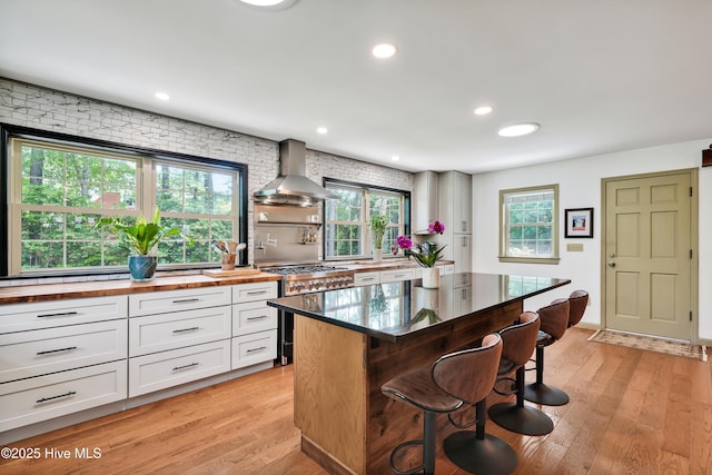 kitchen featuring butcher block counters, high end stove, wall chimney range hood, a kitchen bar, and plenty of natural light