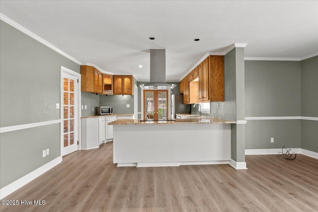 kitchen featuring light wood-style flooring, island exhaust hood, a sink, brown cabinetry, and appliances with stainless steel finishes