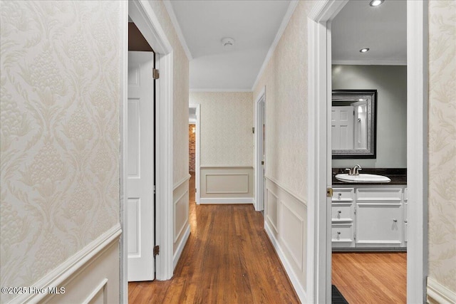hall with wallpapered walls, wood finished floors, crown molding, and a sink
