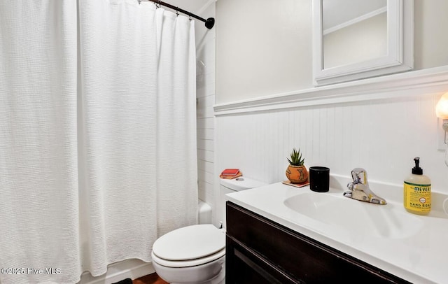 bathroom featuring shower / bath combination with curtain, toilet, vanity, and wainscoting