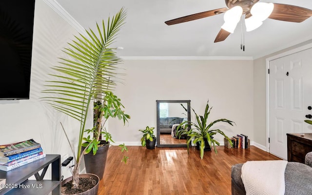 living area featuring baseboards, ornamental molding, wood finished floors, and ceiling fan