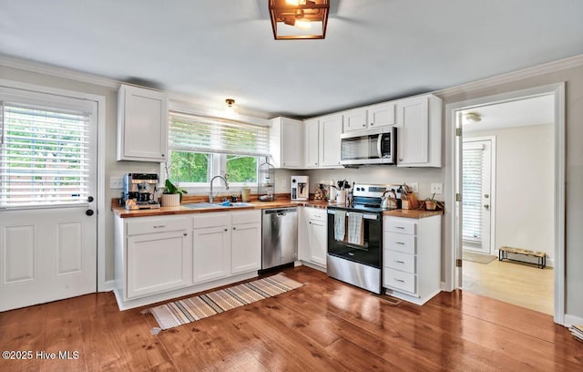 kitchen featuring stainless steel appliances, a sink, wood finished floors, and ornamental molding