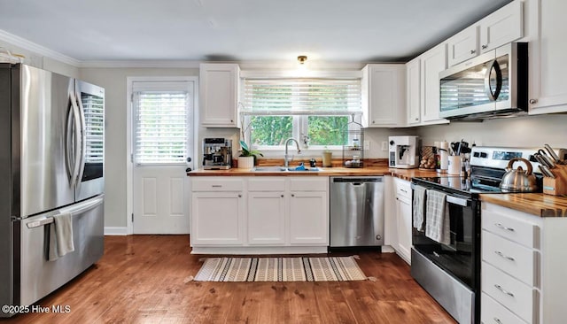 kitchen featuring stainless steel appliances, butcher block counters, a sink, dark wood-type flooring, and white cabinetry