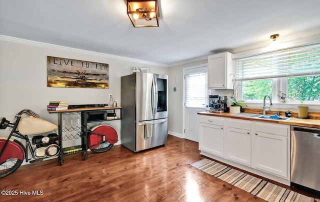 kitchen featuring appliances with stainless steel finishes, a sink, white cabinetry, crown molding, and light wood-style floors