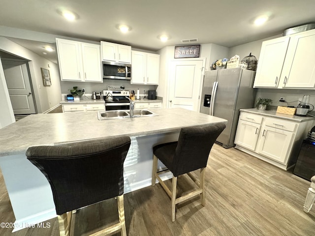 kitchen with white cabinets, stainless steel appliances, light countertops, a sink, and light wood-style flooring