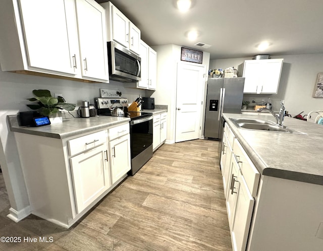 kitchen with visible vents, a sink, light wood-style flooring, appliances with stainless steel finishes, and white cabinetry
