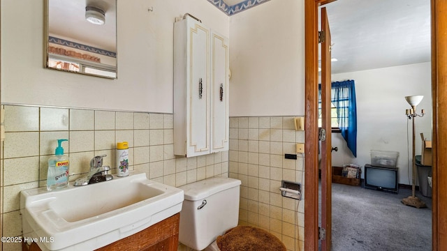 half bath with tile walls, toilet, a wainscoted wall, and a sink