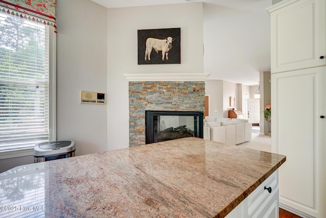 kitchen with light stone counters, a stone fireplace, and white cabinetry