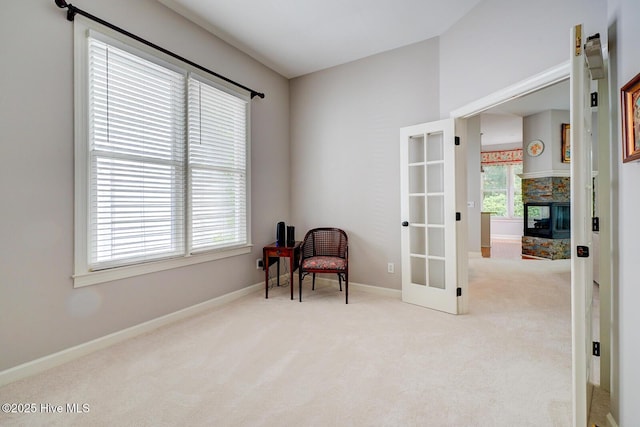 living area featuring carpet floors, french doors, baseboards, and a stone fireplace