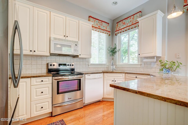 kitchen featuring appliances with stainless steel finishes, white cabinets, light wood-style floors, light stone counters, and decorative backsplash