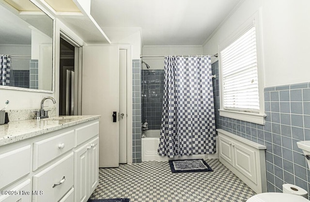 full bath featuring tile patterned floors, shower / bathtub combination with curtain, vanity, tile walls, and wainscoting