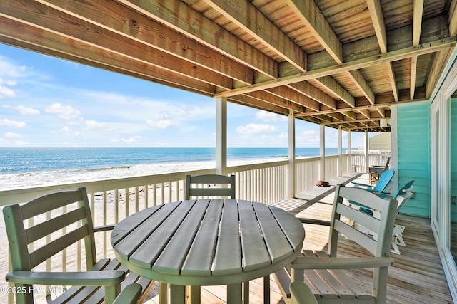 wooden terrace with view of water and beach and outdoor dining area