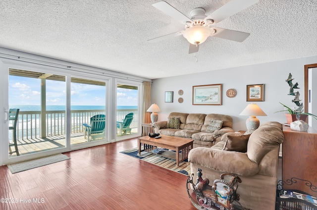 living area featuring a textured ceiling, a water view, ceiling fan, and wood finished floors