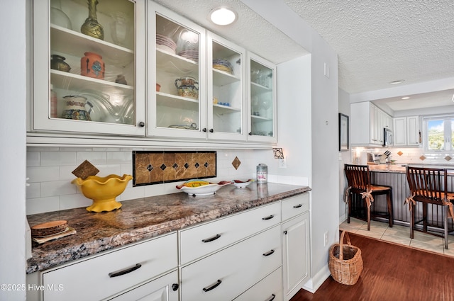 bar with dark wood-style floors, tasteful backsplash, stainless steel microwave, a textured ceiling, and baseboards