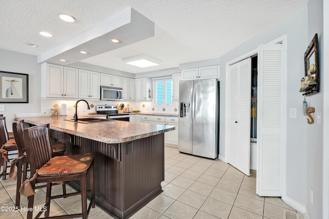 kitchen featuring appliances with stainless steel finishes, a peninsula, a textured ceiling, a sink, and white cabinetry