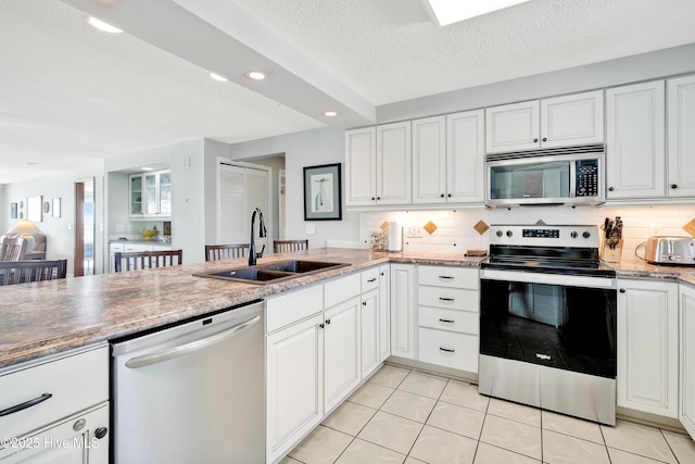 kitchen with stainless steel appliances, a sink, a textured ceiling, tasteful backsplash, and light tile patterned floors