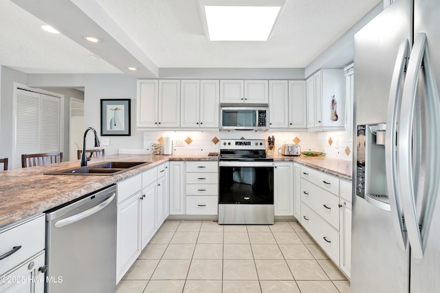 kitchen with stainless steel appliances, a sink, tasteful backsplash, white cabinets, and light tile patterned flooring
