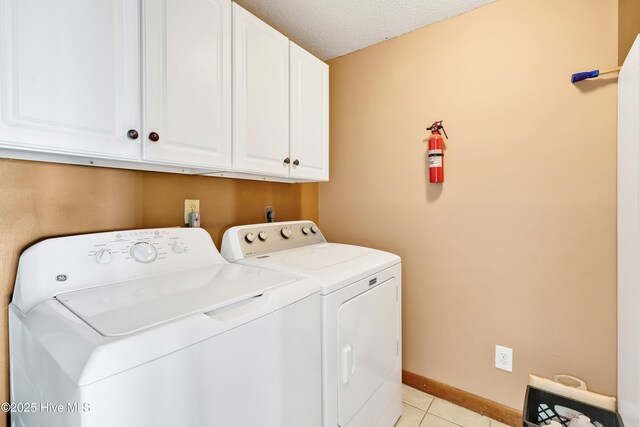 clothes washing area with cabinet space, independent washer and dryer, light tile patterned flooring, a textured ceiling, and baseboards