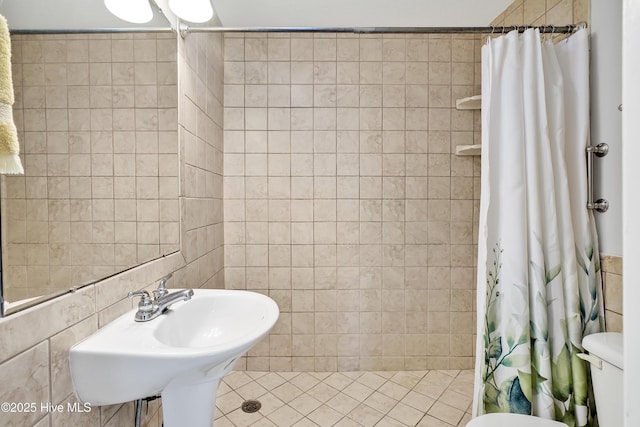 full bath featuring tile walls, a tile shower, toilet, and a sink