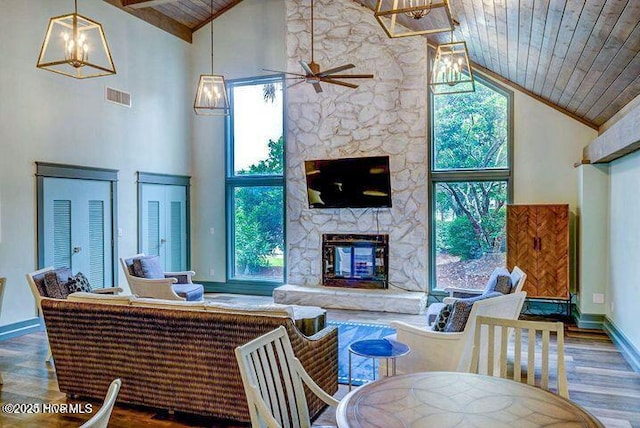 living area featuring high vaulted ceiling, wooden ceiling, wood finished floors, a stone fireplace, and a ceiling fan