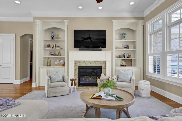 living area featuring baseboards, built in shelves, ornamental molding, and a high end fireplace