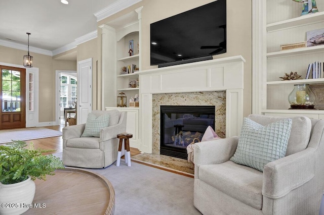 living area with crown molding, baseboards, built in shelves, and a premium fireplace