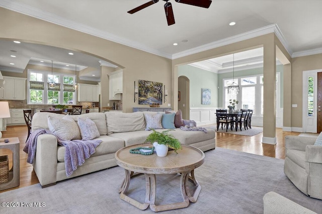 living area with crown molding, arched walkways, ceiling fan with notable chandelier, and light wood-type flooring