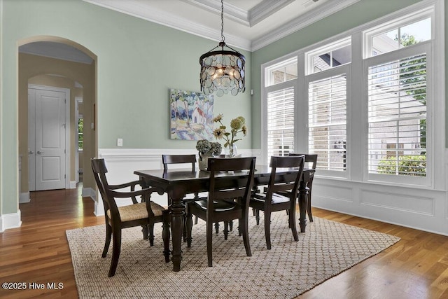 dining space featuring crown molding, arched walkways, wood finished floors, a wainscoted wall, and an inviting chandelier