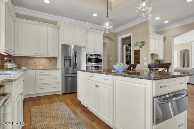 kitchen with a kitchen island, arched walkways, appliances with stainless steel finishes, and a warming drawer