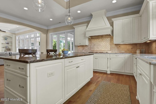 kitchen featuring wood finished floors, custom exhaust hood, a kitchen island, white cabinetry, and arched walkways