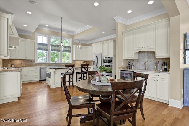 dining area featuring crown molding, light wood finished floors, arched walkways, beverage cooler, and recessed lighting
