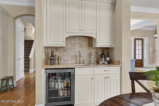 bar featuring crown molding, a sink, beverage cooler, indoor wet bar, and decorative backsplash