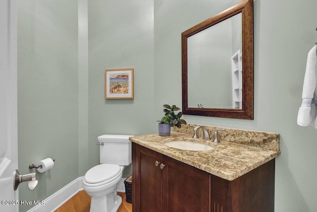 half bath with toilet, baseboards, wood finished floors, and vanity