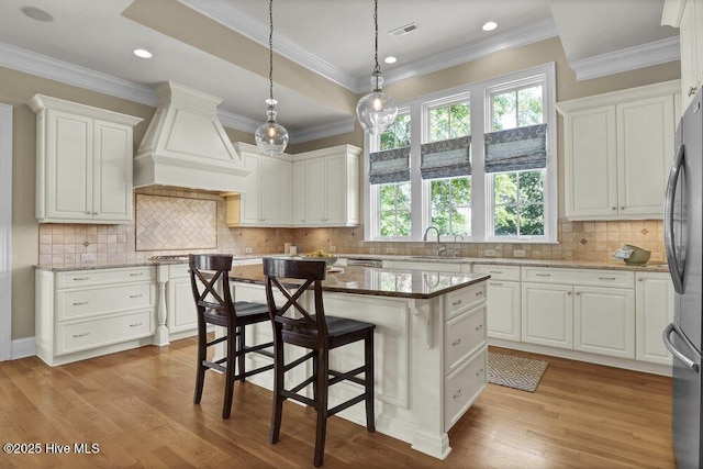 kitchen featuring visible vents, a sink, custom exhaust hood, and white cabinets