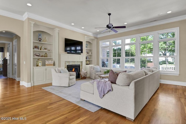 living area featuring baseboards, a ceiling fan, crown molding, and a premium fireplace